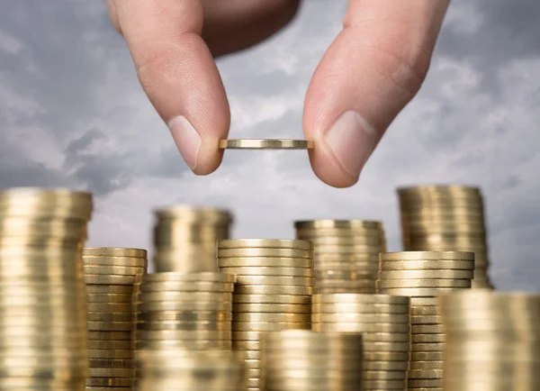 A person holding a coin in front of stacks of coins.